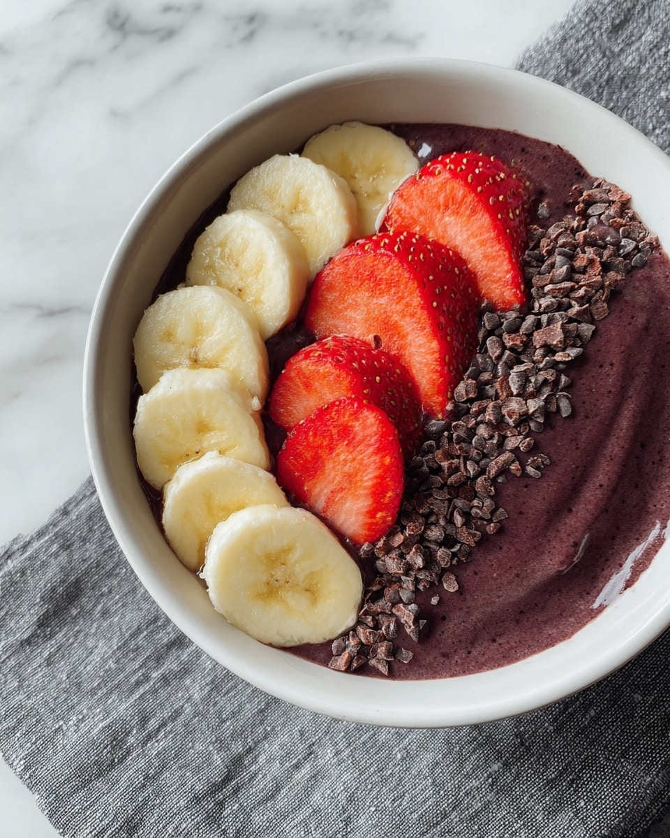 A white bowl filled with smooth, dark purple acai smoothie as the base layer covers the bottom and right side. On the left side, neatly arranged slices of light yellow banana create a curved line. Next to the banana, four bright red, halved strawberries are placed in a row with seeds and texture clearly visible. To the right of the strawberries, there is a line of dark brown, small cocoa nibs adding a rough texture. The bowl rests on a folded gray towel over a white marbled surface. Photo taken with an iphone --ar 4:5 --v 7