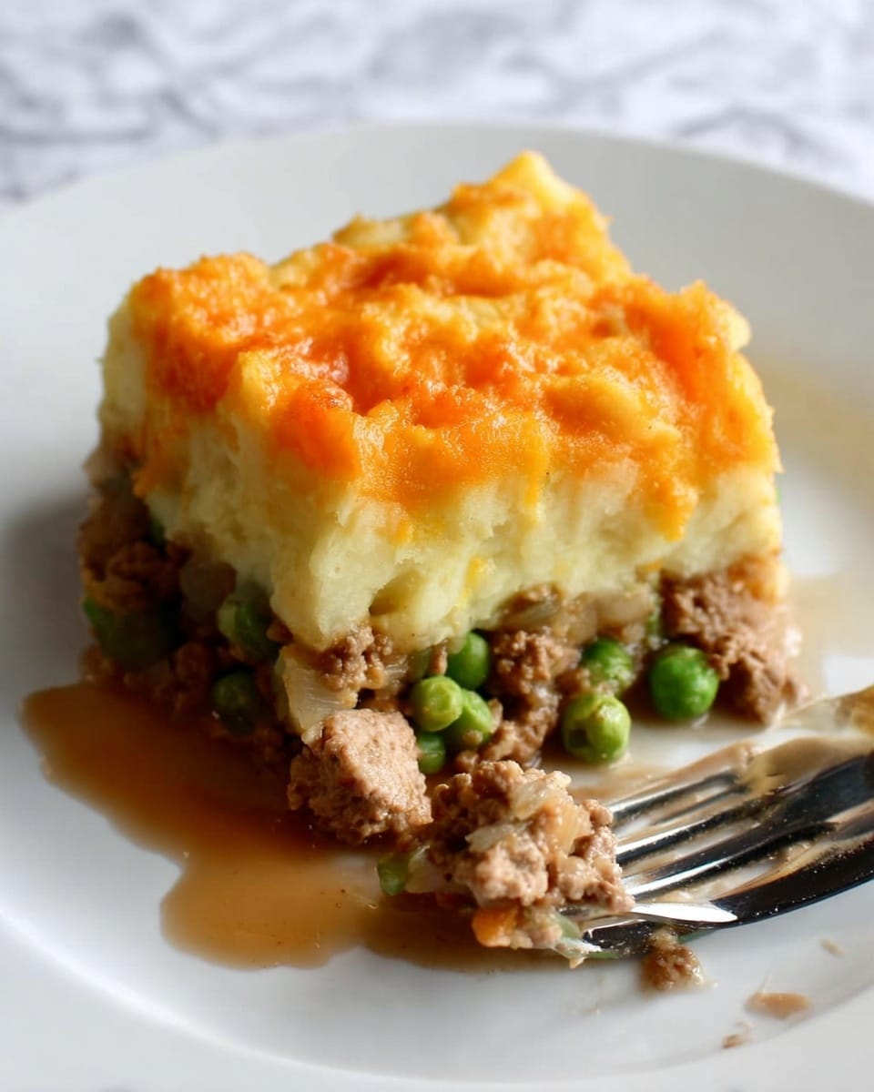The image shows a single square slice of shepherd's pie placed on a white plate with a metal fork beside it tipped at an angle. The pie has three distinct layers: a bottom layer of cooked ground meat mixed with green peas and diced onions in a brown sauce, a middle fluffy layer of pale yellow mashed potatoes, and a top layer covered with melted orange cheddar cheese with a slightly rough texture. The pie appears moist with some sauce around it on the plate. The background is a white marbled texture. Photo taken with an iphone --ar 4:5 --v 7