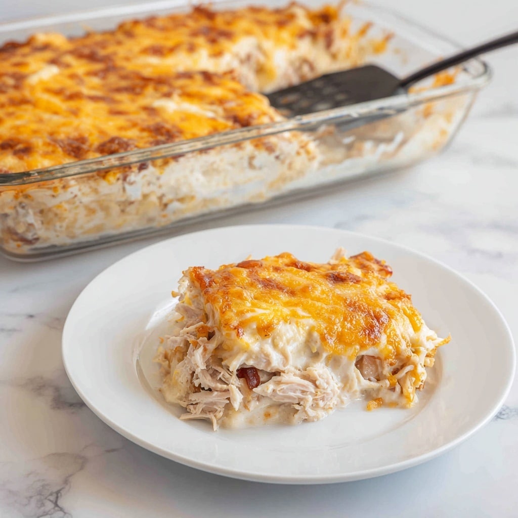 A white plate holds a single serving of a baked casserole with three visible layers: a creamy white sauce base, a middle layer with shredded light brown chicken and light pink ham pieces, and a top layer of melted, golden brown cheese that looks slightly crispy at the edges. Next to the plate is a clear glass baking dish filled with the same casserole, showing a thick layer of gooey cheese covering the chicken and ham inside. A spatula with a black handle rests in the dish, lifting some of the cheesy casserole. The scene is set on a white marbled surface. Photo taken with an iphone --ar 4:5 --v 7