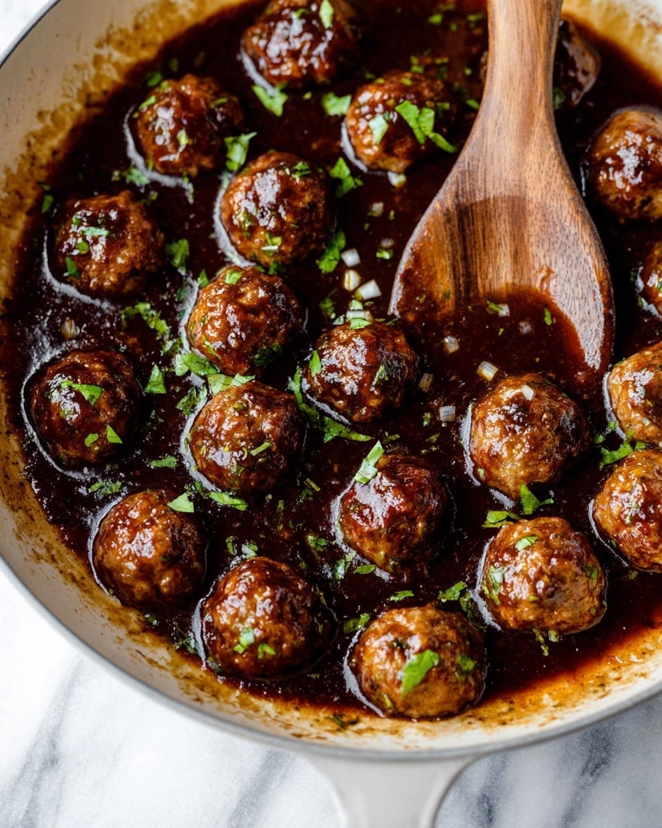 A white plate filled with a pile of small, round meatballs covered in a shiny brown sauce, each meatball showing specks of green herbs inside. The meatballs are garnished with thin strips of fresh green herbs scattered on top. A silver fork is holding one meatball above the plate, highlighting the glossy sauce and textured surface of the meatball. The background is a white marbled texture. photo taken with an iphone --ar 4:5 --v 7