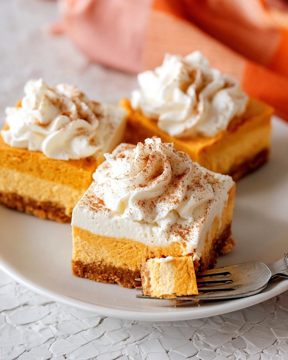 Three square pieces of pumpkin cheesecake on a white plate with a white marbled texture background. Each piece has two layers: a thick, crumbly brown base and a thick, smooth orange pumpkin cheesecake layer on top. Each piece is topped with a thick, swirled layer of white whipped cream sprinkled with a light dusting of cinnamon. In the front, a silver fork holds a bite-sized piece with visible layers, resting on the edge of the plate. The background shows a blurred orange and pink cloth. Photo taken with an iphone --ar 4:5 --v 7