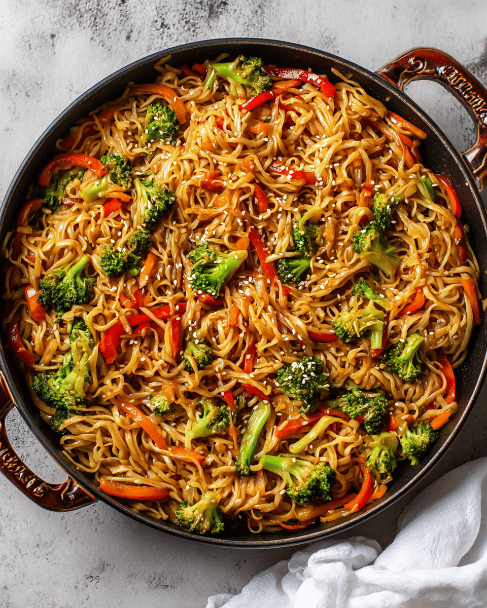 A large round dark pan filled with stir-fried noodles mixed with bright green broccoli pieces, thin orange carrot strips, and red bell pepper slices, all coated in a light brown sauce with some sesame seeds sprinkled on top. The noodles are soft and slightly twisted, layered evenly throughout the pan, while the vegetables add vibrant pops of color and texture. The pan is set on a white marbled surface with a white cloth partially visible on the right side. Photo taken with an iphone --ar 4:5 --v 7