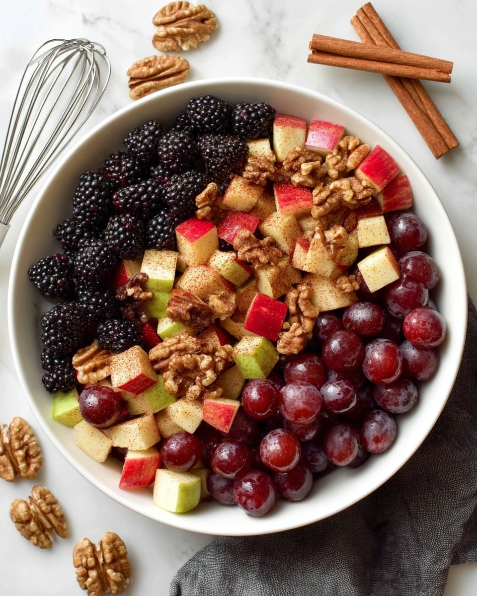 A white bowl filled with a colorful fruit and nut salad, showing three main layers: the base layer is made of fresh black mulberries, the middle layer has round red grapes evenly spread, and the top layer consists of small cubes of red and green apples mixed with whole walnuts, all sprinkled with a light dusting of cinnamon powder. The bowl sits on a white marbled surface with a few walnuts placed around it and cinnamon sticks and a metal whisk positioned nearby. Photo taken with an iphone --ar 4:5 --v 7
