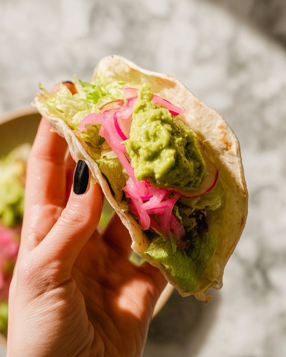 Four quesadilla wedges are arranged in a row on a white speckled oval plate with a thin brown rim, placed on a white marbled surface. Each quesadilla is golden brown on the outside with a soft texture and is topped with shredded lettuce, bright pink pickled onions, chopped green cilantro, and a dollop of chunky green guacamole. Lime wedges are placed on the plate around the quesadillas. To the top right of the plate, there is a small earth-toned bowl containing more guacamole. The light creates soft shadows, enhancing the textures and colors. Photo taken with an iphone --ar 4:5 --v 7