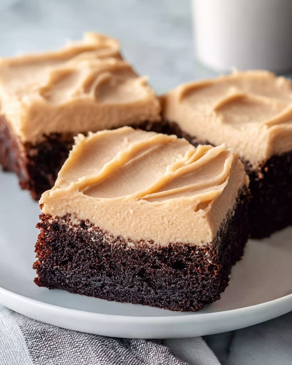 The image shows three square pieces of chocolate cake with a thick layer of light brown frosting on top. Each piece has one even layer of dark, moist chocolate cake at the bottom, and a smooth, creamy frosting layer spread thickly and evenly on top. The cake squares are placed closely together on a white plate that sits on a white marbled surface. The frosting on each piece has subtle swirls and soft peaks, giving it a slightly textured look. The lighting is soft, highlighting the contrast between the dark cake and light frosting. photo taken with an iphone --ar 4:5 --v 7
