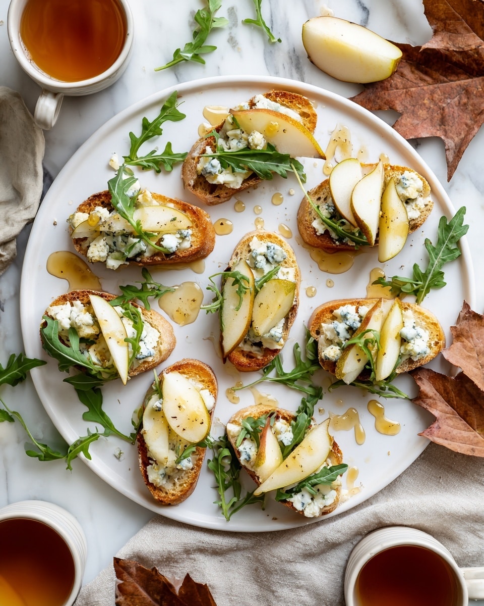 A white round plate with nine small toasted bread slices arranged in a loose circle, each piece topped with a spread of white creamy cheese, thin yellow pear slices, small chunks of blue cheese, and green arugula leaves. Golden honey is drizzled over the toasts and around the plate, adding a shiny texture. The plate sits on a white marbled surface scattered with more arugula leaves and a dried autumn leaf on the right. Two white cups with amber-colored tea and pear slices sit near the edges of the scene, along with a beige cloth in the lower right corner. photo taken with an iphone --ar 4:5 --v 7