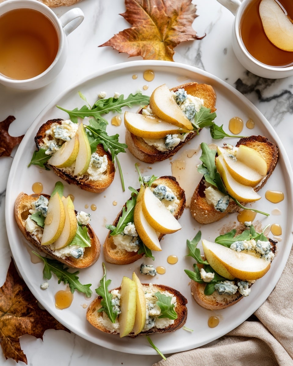 The image shows a white round plate with nine small toasted bread slices. Each slice has a layer of creamy white cheese, topped with two thin yellow pear slices, small chunks of blue cheese, and a couple of green arugula leaves. Light brown honey is drizzled over the bread and plate, with some droplets scattered around. The plate rests on a white marbled surface with an autumn leaf, a beige cloth, and two white cups of tea with pear slices visible in the background. photo taken with an iphone --ar 4:5 --v 7