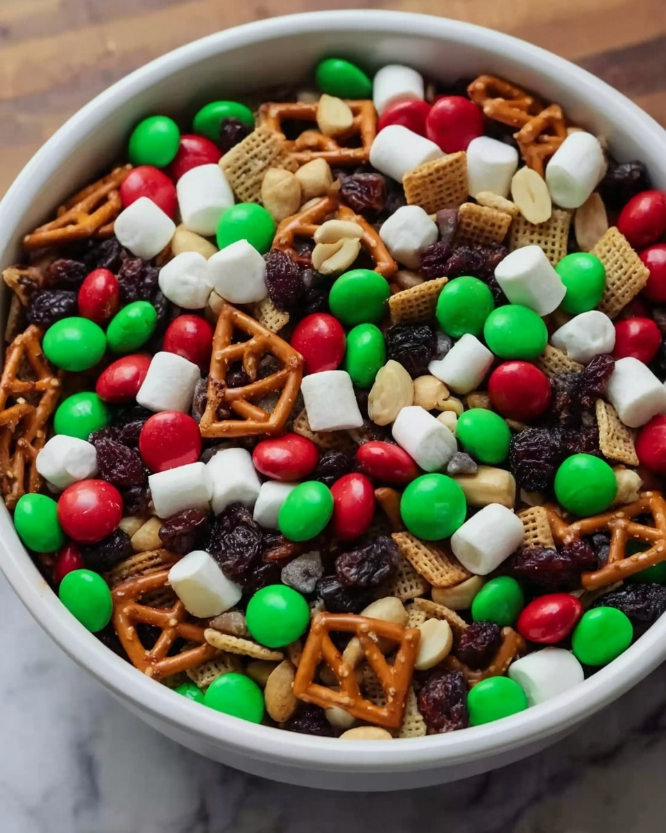 The image shows a close-up of a large white bowl filled with a colorful trail mix. The mix includes small red, green, and brown candy-coated chocolates, white mini marshmallows, light brown peanuts, dark raisins, and golden pretzel squares. The bowl is full, showcasing the varied textures from smooth candy shells to rough pretzels and soft marshmallows. The bowl sits on a white marbled surface, with parts of the wooden table visible beneath. photo taken with an iphone --ar 4:5 --v 7