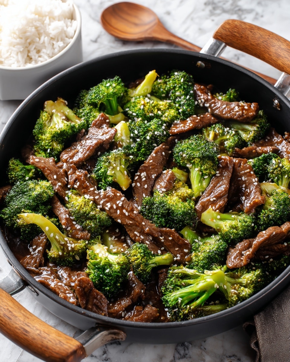 A black pan with wooden handles is filled with beef and broccoli stir-fry. The dish has two main layers: bright green broccoli florets with a slightly glossy texture, evenly mixed with tender, thin strips of dark brown beef coated in a shiny sauce, sprinkled lightly with white sesame seeds. The background shows a small white bowl of steamed rice placed on a white marbled surface next to the pan, along with a wooden spoon resting near the pan. Photo taken with an iphone --ar 4:5 --v 7