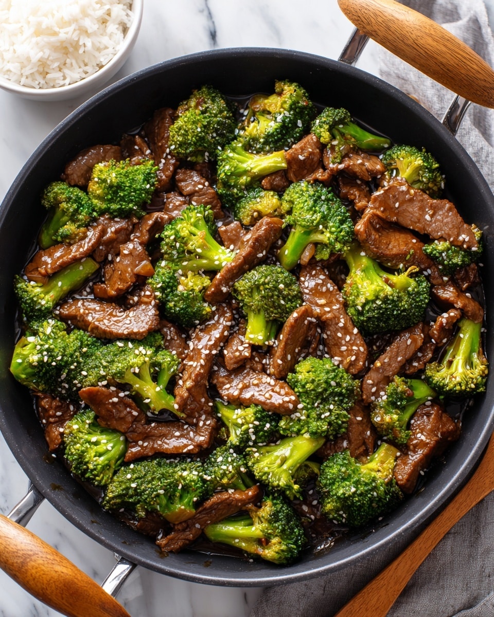 A close-up of a black pan with wooden handles, filled with beef and broccoli stir fry. The dish has bright green broccoli florets mixed evenly with brown beef strips coated in a shiny sauce, sprinkled lightly with white sesame seeds. The pan sits on a white marbled surface, with a small white bowl of white rice placed beside it in the top left corner, and a wooden spoon resting on the right. photo taken with an iphone --ar 4:5 --v 7