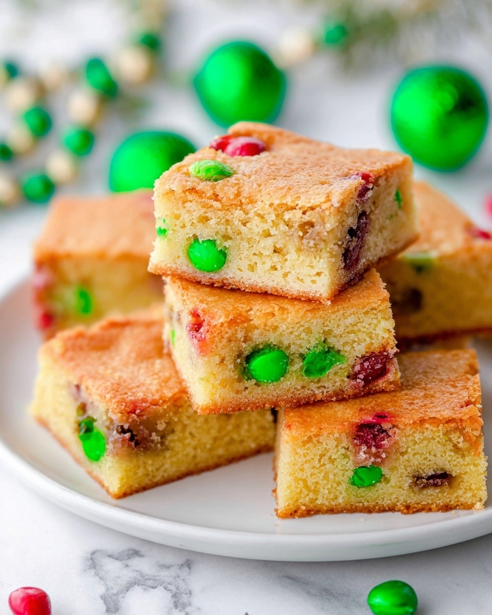 A white plate stacked with several square blondie bars, each bar showing two layers: a soft, light golden-brown cake layer on top and bottom with a pale yellow crumb inside. The blondies contain colorful small candy pieces, mainly red and green, embedded both on the surface and inside. The texture looks moist and slightly crumbly. Some candies melt slightly, spreading bright green and red spots inside the blondie. The plate sits on a white marbled surface, with blurred green decorative elements and Christmas beads nearby. Photo taken with an iphone --ar 4:5 --v 7