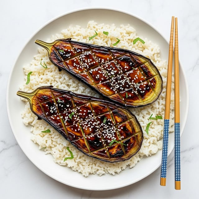 Two grilled eggplant halves lie on a bed of white rice inside a white bowl. Each eggplant half has a shiny, dark purple skin with golden brown and black grill marks across the surface. The flesh of the eggplants is soft and has a rich, glazed look with a sticky caramel color sauce spread evenly in a crisscross pattern. Sprinkles of white sesame seeds and small chopped green herbs are scattered on top, adding texture and color contrast. Next to the bowl, a pair of wooden chopsticks with blue and white patterned handles rest on the white marbled surface. photo taken with an iphone --ar 4:5 --v 7
