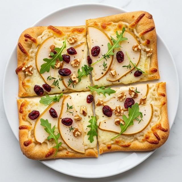 The image shows a flatbread pizza on a white plate with a thin, golden-brown crust. The pizza has a layer of melted cheese topped with thin slices of pear, scattered small red dried cranberries, and chopped walnuts. Green fresh herbs like arugula leaves and small thyme sprigs are sprinkled on top, adding a touch of color contrast. The texture of the cheese looks smooth and slightly bubbly, and the pear slices are soft with a pale yellow color edged with light brown. The pizza is cut into four rectangular pieces and placed on a white marbled surface. Photo taken with an iphone --ar 4:5 --v 7