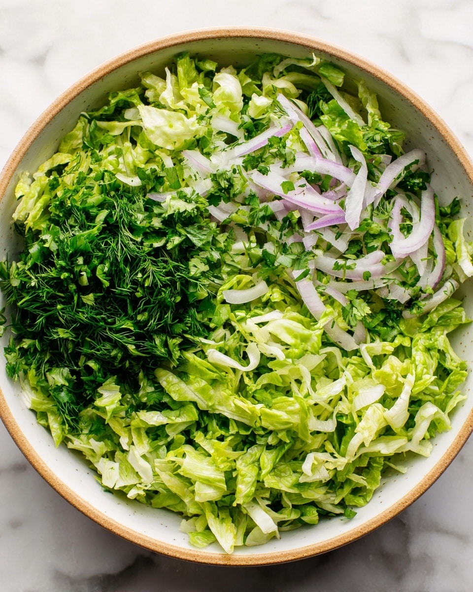 The image shows a close-up of a fresh salad in a white bowl with a light brown rim, placed on a white marbled surface. The salad has several layers, starting with a base of torn green lettuce leaves that show various shades of light and dark green. On top of the lettuce, there are thin slices of light purple onion, small pieces of white cheese, and finely chopped herbs in dark green shades. The textures vary from soft and leafy to slightly crunchy with the onions. The photo was taken with an iphone --ar 4:5 --v 7