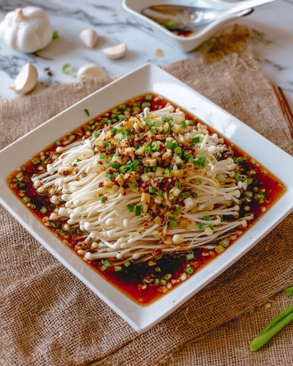 The image shows a white square plate filled with a dish of enoki mushrooms. The mushrooms form the base layer with their thin, long white stems and small caps, covering most of the plate. They are topped with a reddish-brown soy-based sauce that pools around the edges, creating a glossy wet texture. Scattered over the mushrooms and sauce are small chopped green onions and bits of cooked garlic or chili that add a mix of green and golden brown colors as the final layer. The plate is set on a rustic brown burlap cloth over a white marbled surface, with garlic cloves and a white square dish holding a spoon and chopsticks visible in the background. Photo taken with an iphone --ar 4:5 --v 7