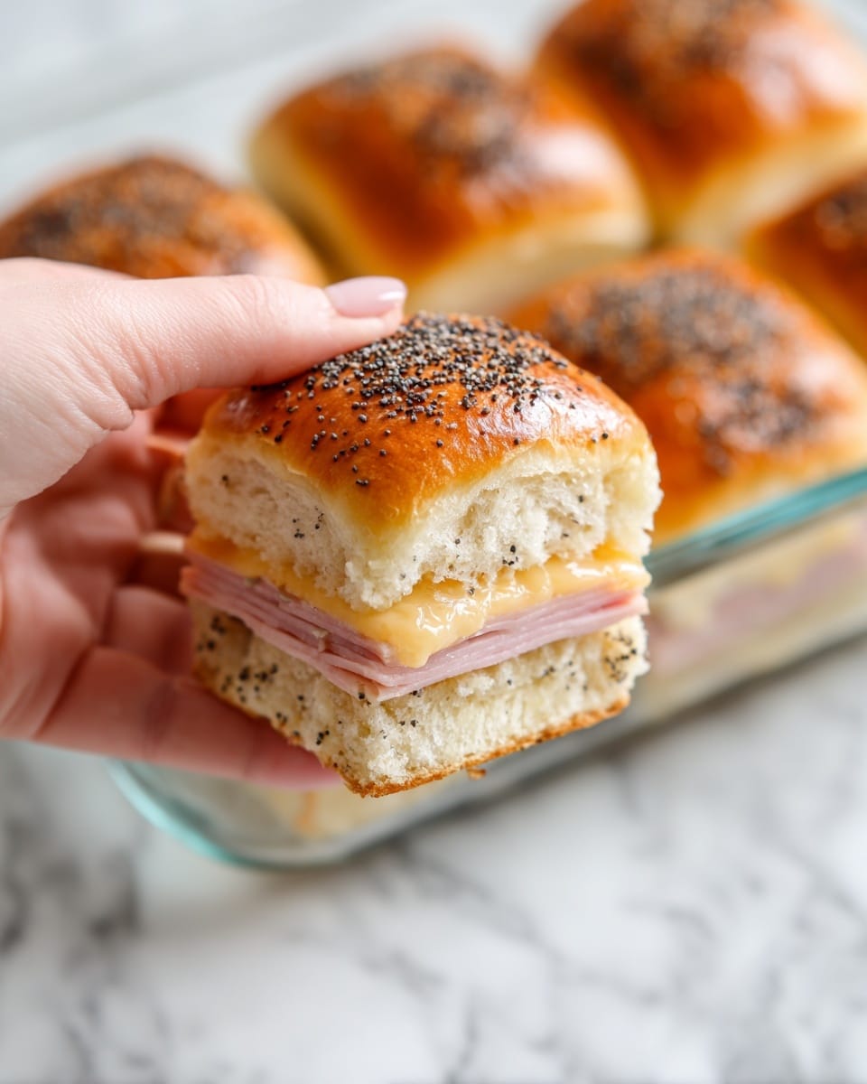 A close-up view of a small sandwich being held by a woman's hand, showing three layers: a shiny golden-brown top bread sprinkled with black poppy seeds, a thin pale pink layer of ham in the middle, and a soft light beige bottom bread layer. The sandwich has a glossy texture with some melted cheese or butter visible along the edges. In the background, more of the same sandwiches are seen in a clear glass baking dish on a white marbled surface. The photo taken with an iphone --ar 4:5 --v 7