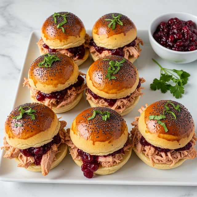The image shows six small sandwiches arranged in two rows on a long white rectangular plate placed on a white marbled surface. Each sandwich has a glossy golden-brown top bun sprinkled with black poppy seeds. Below the top bun, there is a layer of shredded light brown pulled meat mixed with a deep red sauce, layered over a bottom white bun. Small fresh green herb sprigs, likely thyme, are scattered on and around the sandwiches for decoration. To the side, there is a small white bowl filled with the same deep red sauce. The photo taken with an iphone --ar 4:5 --v 7