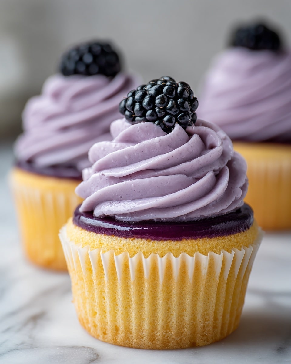 The image shows a close-up of a cupcake with three main layers. The bottom layer is the golden-yellow cupcake base inside a purple ribbed wrapper. On top of the cupcake is a smooth, dark purple glossy jam layer. Above the jam is a large swirl of light purple whipped frosting with a soft, creamy texture. At the very top, there is one large, shiny black blackberry fruit. The background has a white marbled texture, and part of a woman's hand is gently reaching for one cupcake. Photo taken with an iphone --ar 4:5 --v 7