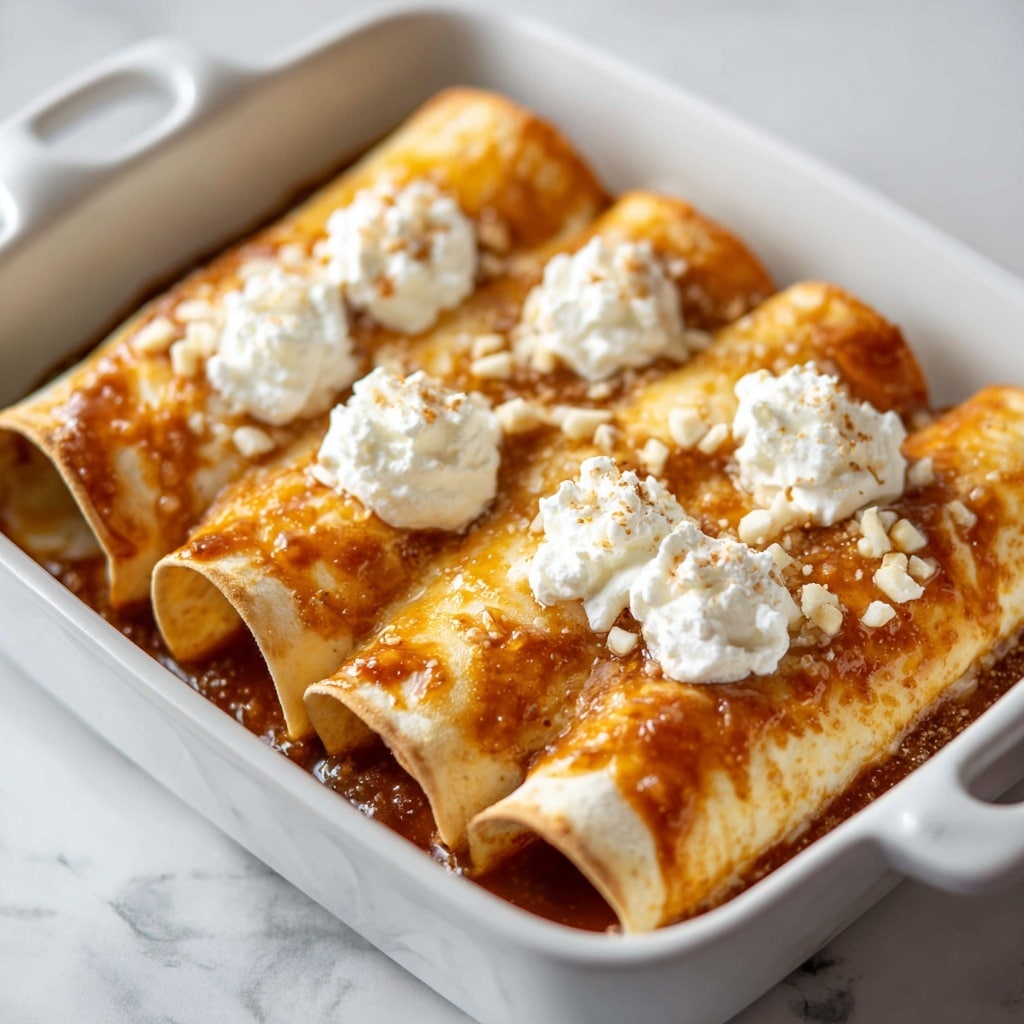 The image shows three rolled enchiladas placed side by side in a dark baking dish on a white marbled surface. Each enchilada is covered with a shiny, golden brown sauce drizzled in thin lines across the length. On top of the sauce, there are small white cheese pieces and a light sprinkle of chopped green herbs adding color contrast. The tortillas have a soft, slightly toasted texture with some browning along the edges. The overall look is warm and appetizing, with a close-up focus that highlights the melted cheese and herb garnish. Photo taken with an iphone --ar 4:5 --v 7