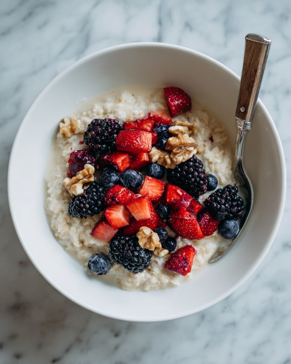 A white bowl filled with creamy oatmeal forms the base layer, light beige in color with a soft, slightly lumpy texture. On top, a scattered layer of bright red chopped strawberries, deep blue blueberries, and dark purple-black blackberries adds vibrant color and freshness. Small pieces of light brown walnuts are sprinkled among the berries, adding crunch and a rustic feel. A silver spoon with a wooden handle rests inside the bowl, partially submerged in the oatmeal. The bowl is placed on a white marbled surface. photo taken with an iphone --ar 4:5 --v 7