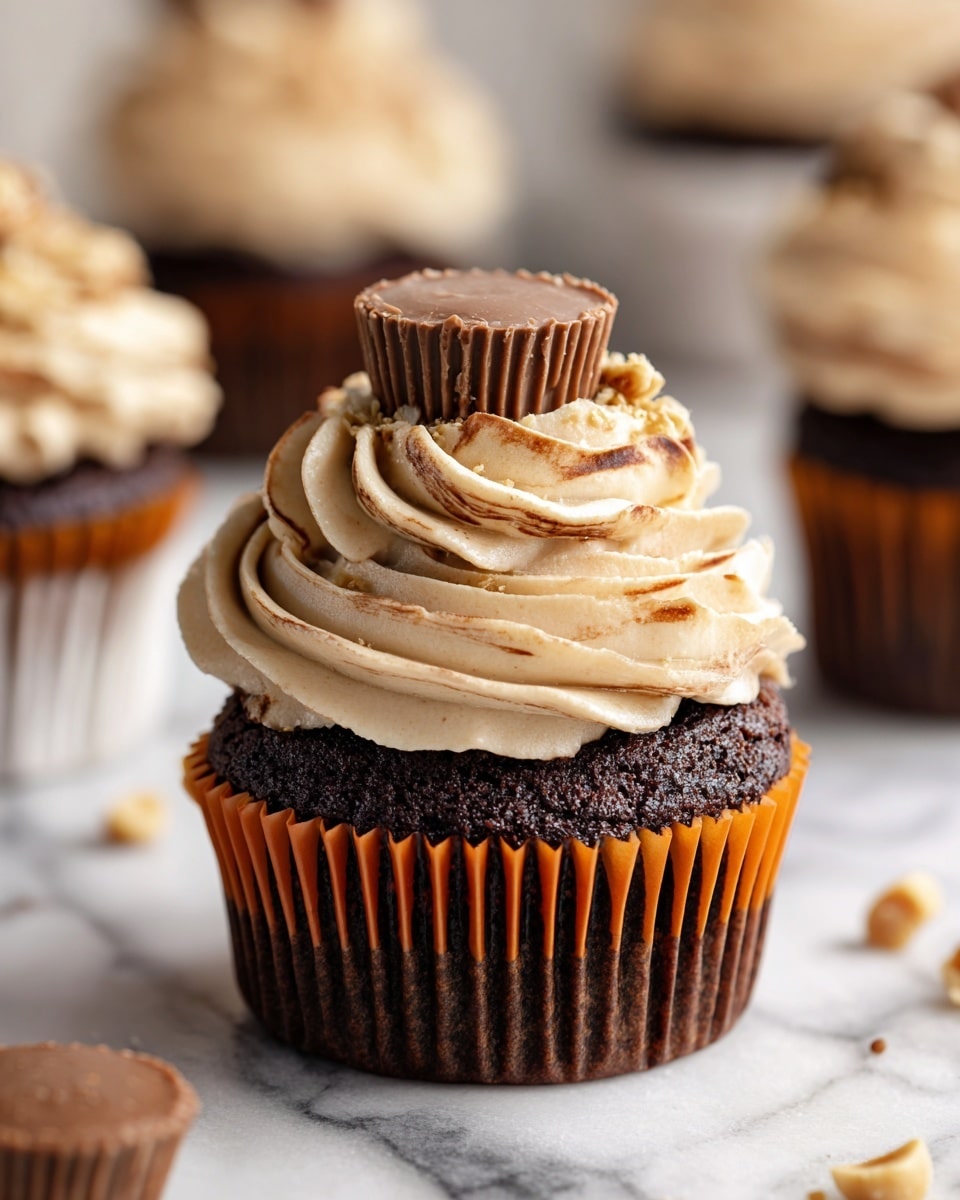 A rich chocolate cupcake sits in an orange liner, topped with a swirl of light tan and chocolate brown frosting that looks creamy and fluffy. On top of the frosting, a large round milk chocolate peanut butter cup is placed upright, adding a smooth and shiny texture contrast. The cupcake is set on a white marbled surface with some scattered cashew nuts around it, and blurry cupcakes in the background for depth. photo taken with an iphone --ar 4:5 --v 7