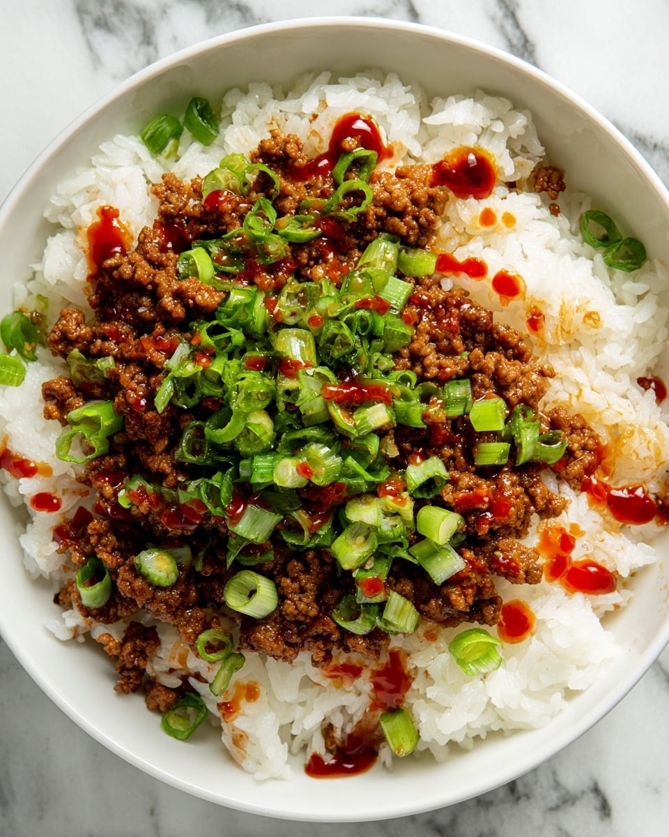A close-up of a dish in a white bowl filled with fluffy white rice as the base layer, topped with a layer of browned ground meat mixed with small bits of vegetables. The meat layer is covered with scattered pieces of chopped green onions and small drops of a red, sauce-like garnish. The textures show the soft rice underneath and the slightly crispy, crumbly meat with fresh, bright green onions on top. The background is a white marbled surface. Photo taken with an iphone --ar 4:5 --v 7