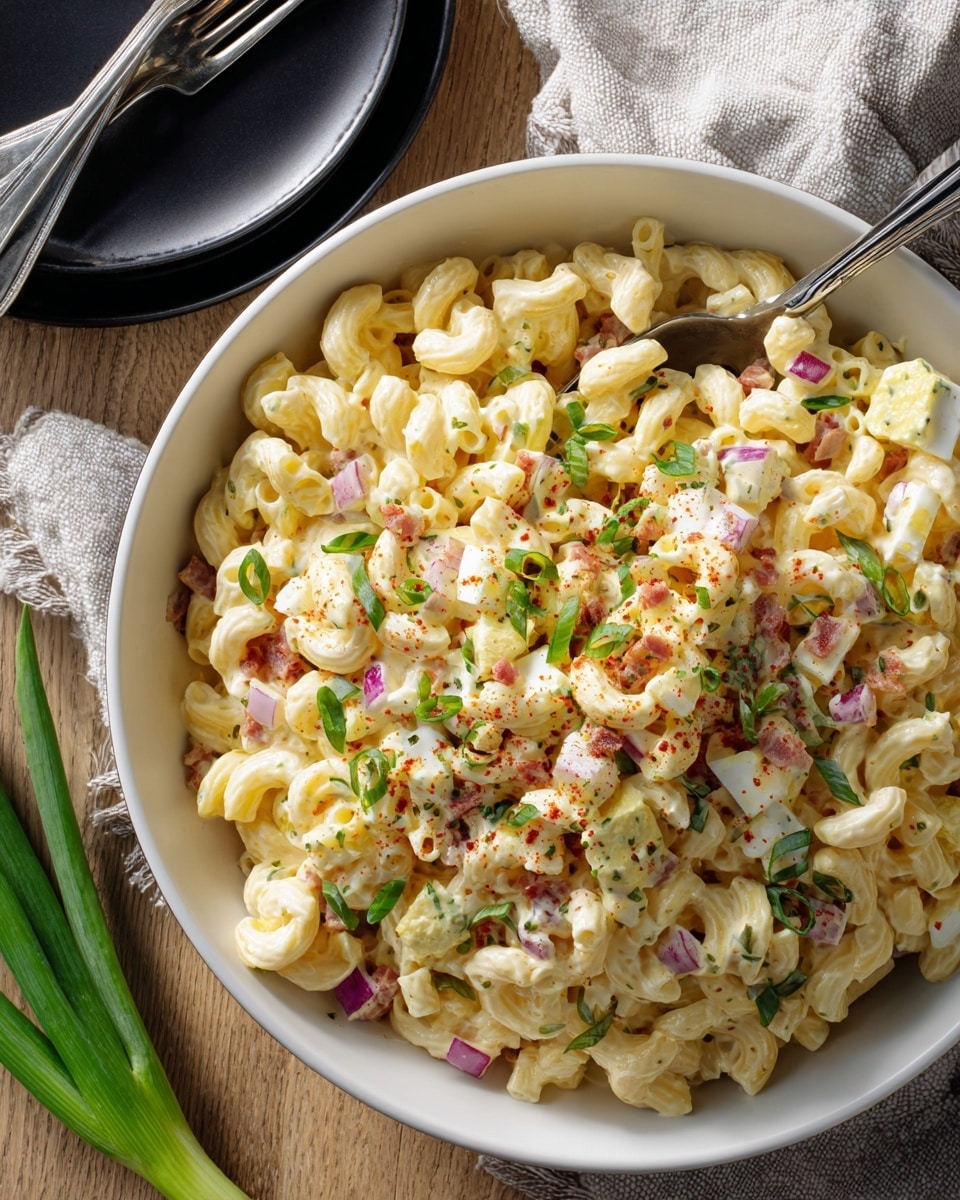 A large white bowl filled with creamy macaroni salad sits on a white marbled texture, the salad consisting of pale yellow macaroni mixed with chunks of hard-boiled egg and finely chopped red onion, giving it spots of white and purple. Small pieces of crispy red bacon are scattered on top, along with bright green sliced scallions and a light dusting of red paprika powder adding color contrast. A black spoon is partially buried in the salad, resting on the edge of the bowl. Near the bowl, a small black plate holds two silver forks and fresh green scallions lie nearby. photo taken with an iphone --ar 4:5 --v 7