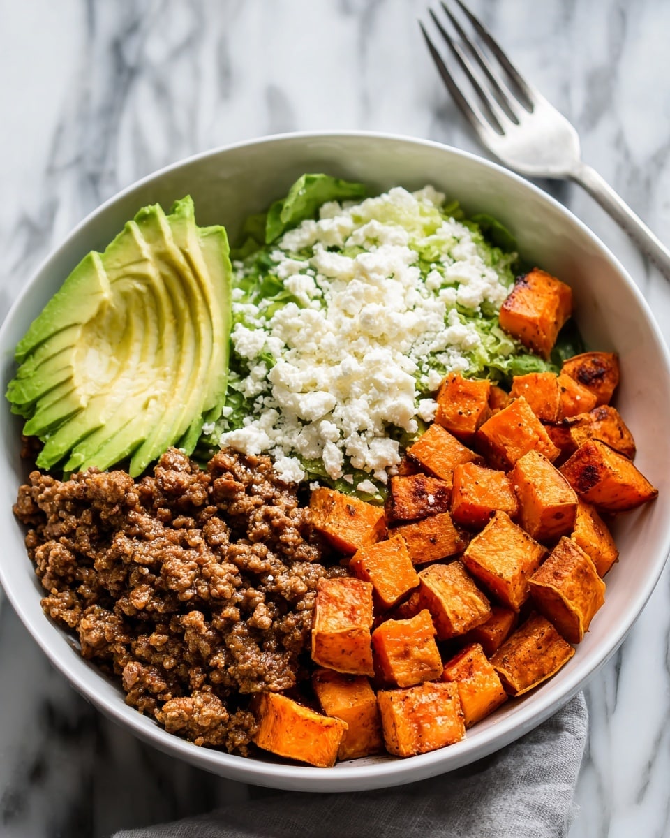 A white bowl on a white marbled surface filled with four distinct layers arranged side by side: bright orange roasted cubed sweet potatoes with a slightly crispy outside, a ground beef mix cooked in a reddish sauce, thinly sliced green avocado fanned out, topped with a layer of crumbled white cheese, and small bits of fresh lettuce peeking from behind. A shiny metal fork rests near the top edge of the bowl. The photo taken with an iphone --ar 4:5 --v 7