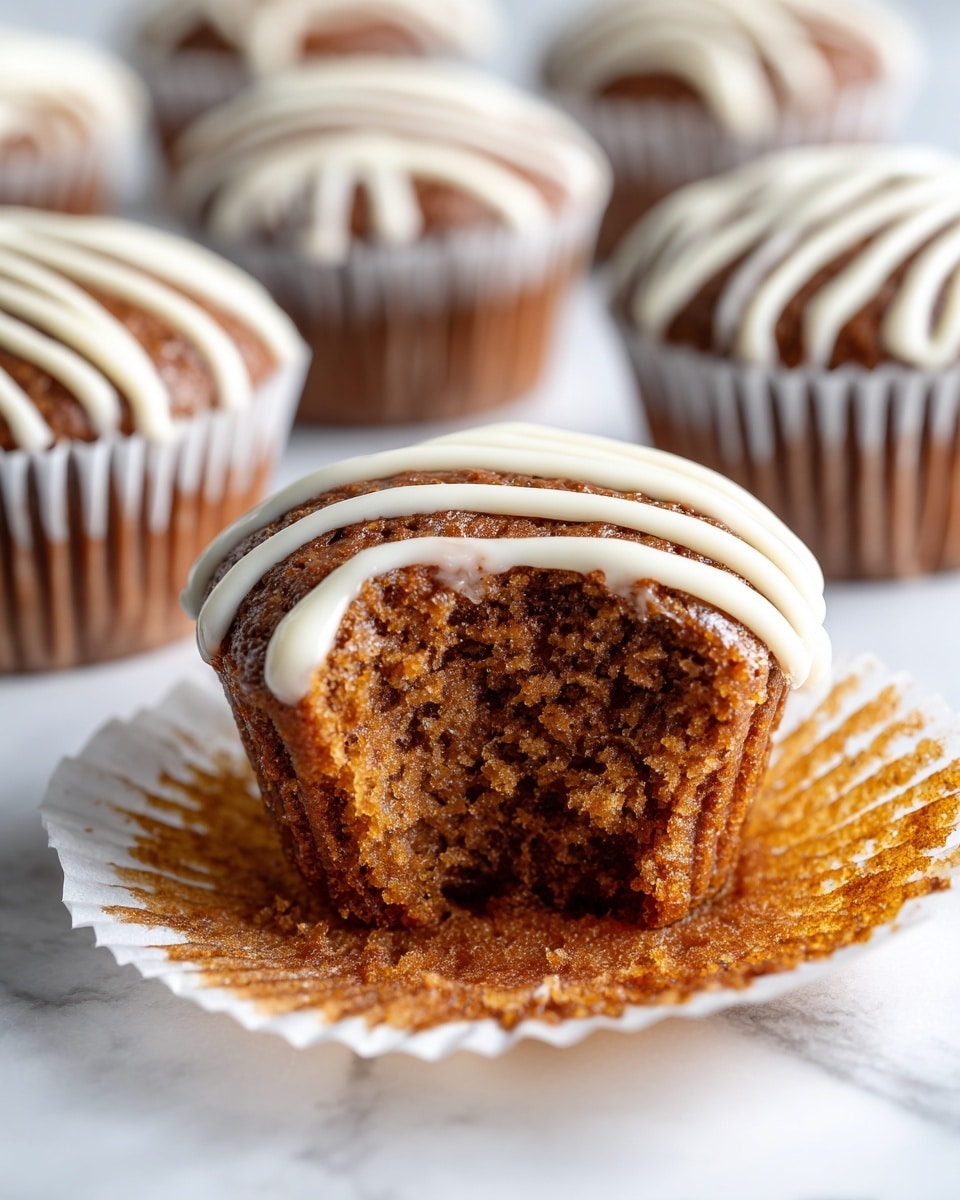 The image shows a close-up of a brown cupcake with a moist, soft texture and small air holes visible inside where a bite has been taken out. The top of the cupcake is crowned with a thick drizzle of smooth white icing that slightly drips down the sides. In the background, there are several similar cupcakes, each topped with white icing in a wavy pattern. All cupcakes are wrapped in white paper liners. They sit on a white marbled surface with soft lighting that highlights the warm tones and textures of the cupcakes. photo taken with an iphone --ar 4:5 --v 7