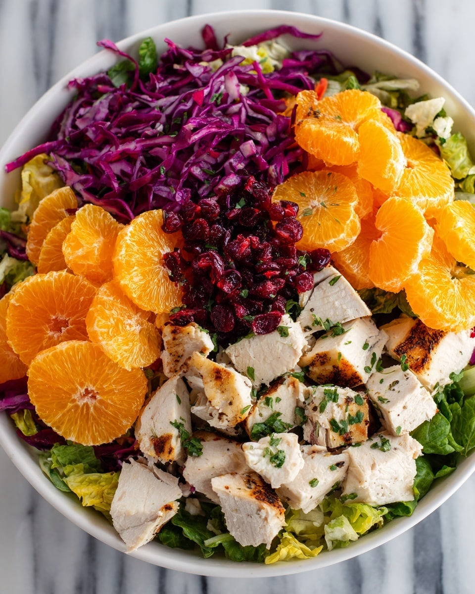 A bowl filled with a colorful mixed salad showing three main layers: the bottom layer of green leafy lettuce and some bright purple cabbage pieces, the middle layer of orange slices scattered evenly, and the top layer of thick white chicken chunks mixed with small red dried berries and green herbs sprinkled on top. The bowl is white, and the background shows a white marbled texture. photo taken with an iphone --ar 4:5 --v 7