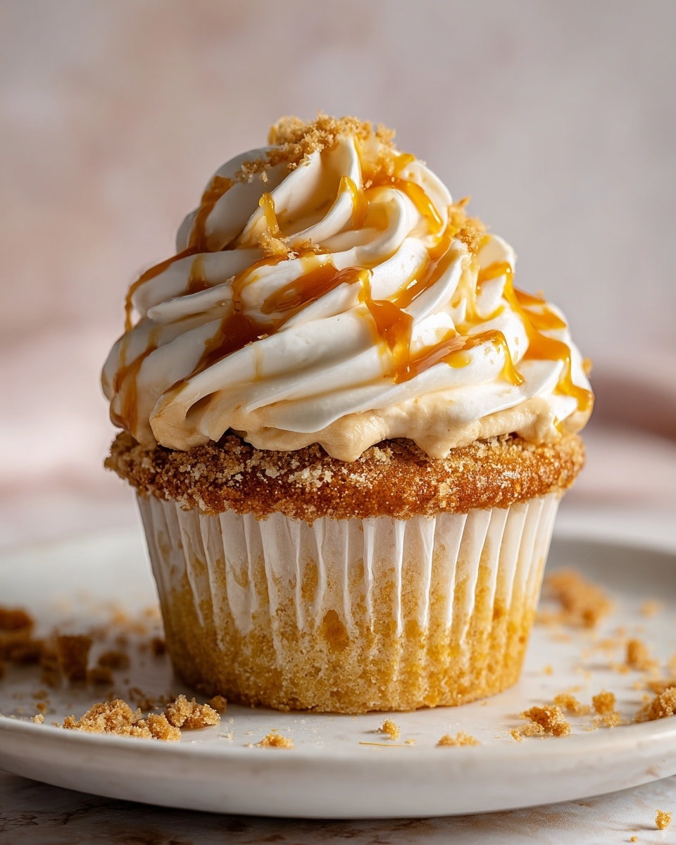 A single cupcake is shown close up on a white plate with some crumbs scattered around. The cupcake has a golden brown base with a textured surface inside a white paper liner. On top, there are two layers of creamy white frosting piped in a swirl with a smooth texture. The frosting is drizzled with light caramel sauce and sprinkled with fine orange crumbs, adding color and texture contrast. The background is a white marbled texture, creating a clean and simple setting. photo taken with an iphone --ar 4:5 --v 7