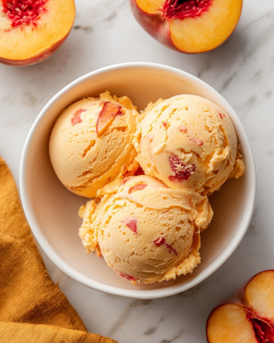 A white bowl filled with three nearly round scoops of creamy, light peach-colored ice cream with visible small chunks of peach scattered throughout, creating a textured surface. The bowl rests on a white marbled surface with a sliced peach showing yellow-orange flesh with a red center placed nearby. A mustard-yellow cloth is partially visible at the bottom. The image captures the ice cream’s soft, smooth texture with a slightly melting look. Photo taken with an iphone --ar 4:5 --v 7