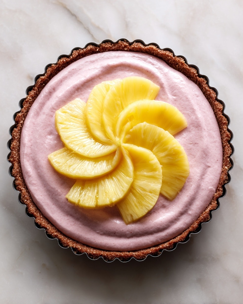 The image shows a pie with three clear layers: the bottom crust is brown and crumbly with a rough texture, holding the pie together in a round pan with fluted edges; the middle layer is a thick, smooth, light pink cream spread evenly across the crust; on top, there are six bright yellow pineapple slices arranged in a circular pattern, creating a flower-like shape. The pie sits on a white marbled surface. photo taken with an iphone --ar 4:5 --v 7