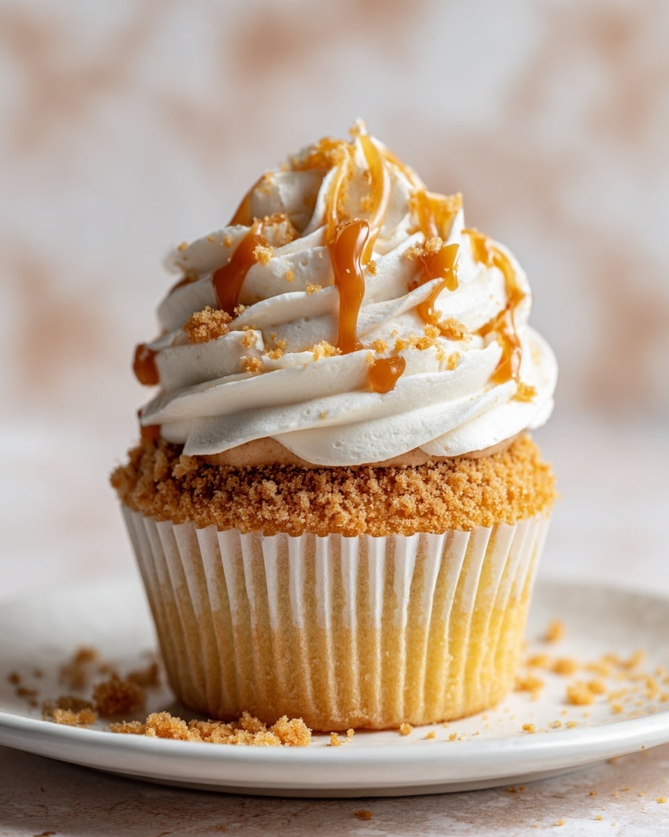 The image shows a close-up view of a single cupcake on a white plate with a white marbled texture background. The cupcake has three visible layers: the base layer is a golden-brown sponge cake with a slightly rough texture and crinkled edges inside a white crinkled paper cup; the middle layer is a smooth light brown frosting with a creamy look, spread thinly above the cake; the top layer is a thick swirl of white whipped frosting with a soft, fluffy texture, drizzled with caramel sauce in thin lines, and sprinkled with crumbs of the golden cake. There are also crumbs scattered around on the plate, adding some texture detail. photo taken with an iphone --ar 4:5 --v 7