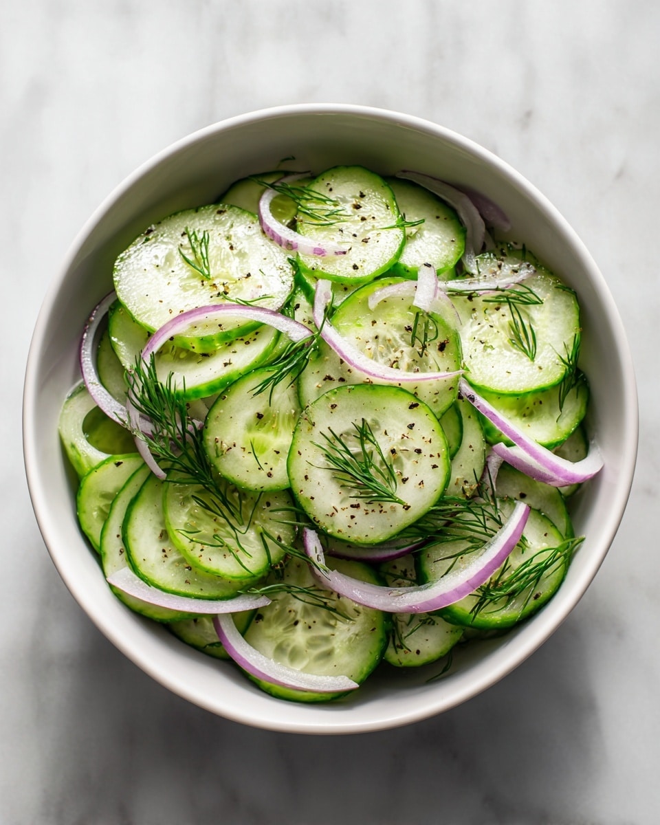 A white bowl filled with thinly sliced cucumber rounds layered evenly, showing their light green color and watery texture. Mixed throughout are thin, curly slices of red onion that add a muted purple touch. Small sprigs of fresh dill are scattered on top, adding fine green details and a fresh look. The salad appears lightly dressed, with a slight shine on the cucumber slices, and there is a simple sprinkle of black pepper for contrast. The bowl is placed on a white marbled surface, with soft natural light emphasizing the freshness of the ingredients. Photo taken with an iphone --ar 4:5 --v 7