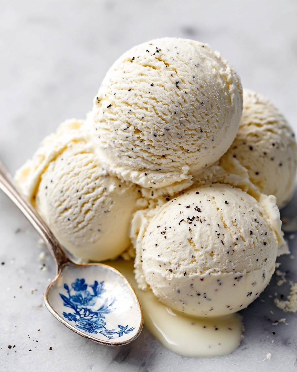 Three scoops of creamy white vanilla ice cream with tiny black vanilla bean specks sit closely together on a white plate placed on a white marbled surface. A silver spoon with a blue floral pattern on the handle is lifting one scoop slightly, showing the smooth and soft texture of the ice cream. Some melted ice cream pools gently around the scoops, enhancing the rich, creamy look. photo taken with an iphone --ar 4:5 --v 7