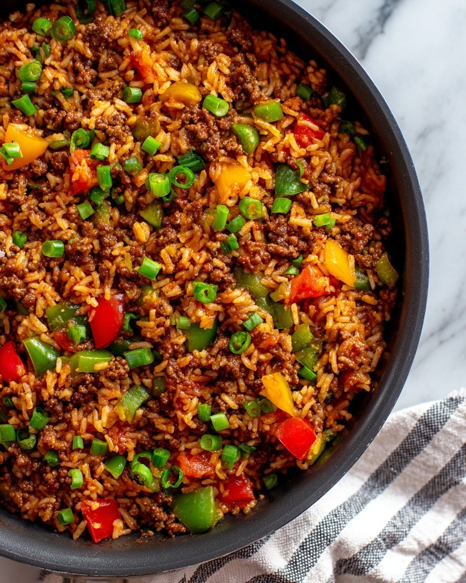A close-up view of a large black pan filled with a colorful mix of cooked ground beef, fluffy rice, and chopped bell peppers in green, red, and yellow. The dish looks moist and well-cooked with the rice and beef evenly mixed, and the peppers adding bright spots of fresh color throughout. Small onion pieces and bits of tomato are also visible, blending well into the mixture. The pan is resting on a white marbled surface with a striped cloth partially visible at the base, and the scene is warmly lit to show the rich textures and colors of the meal. photo taken with an iphone --ar 4:5 --v 7
