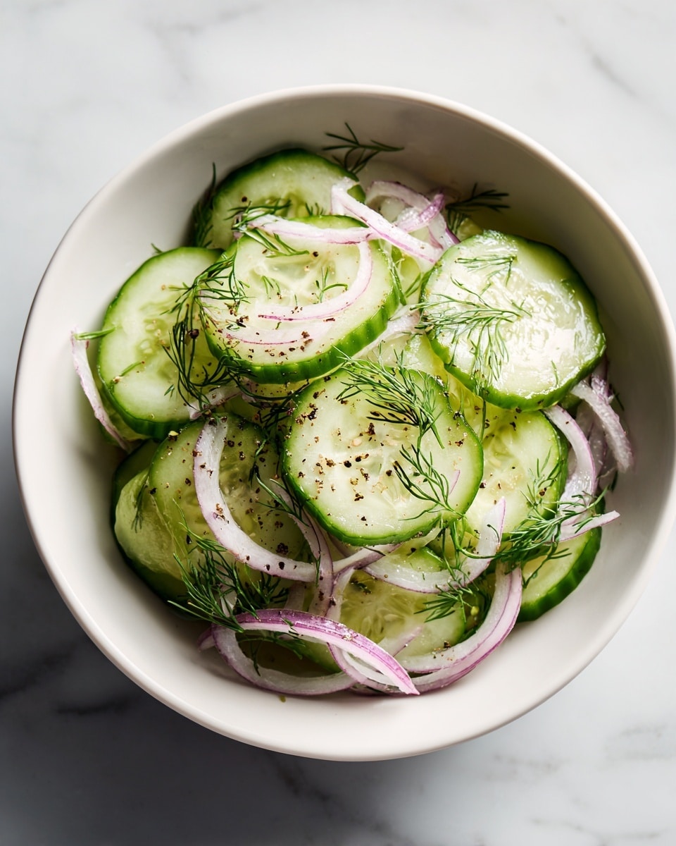 A white bowl filled with thin round slices of bright green cucumber layered evenly. Interspersed within the cucumber slices are thin curved strips of light purple onion. Small sprigs of fresh green dill lie on top and between the layers, sprinkled with coarse black pepper for texture. The bowl sits on a white marbled surface with soft lighting highlighting the fresh, crisp ingredients. photo taken with an iphone --ar 4:5 --v 7