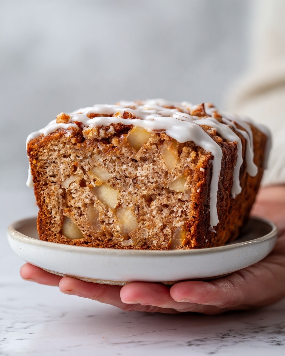 The image shows a loaf of spiced apple fritter bread with a golden brown crust on a white marbled surface. The bread has several visible layers inside: light brown dough mixed with small chunks of soft yellow apple, and a swirl of cinnamon spice running through the middle. On top, white icing is drizzled thickly over the crust, with parts dripping down the sides, adding a shiny, smooth texture that contrasts with the rough bread surface. A woman's hand is gently touching the loaf near one corner, showing the size and texture of the bread. Photo taken with an iphone --ar 4:5 --v 7