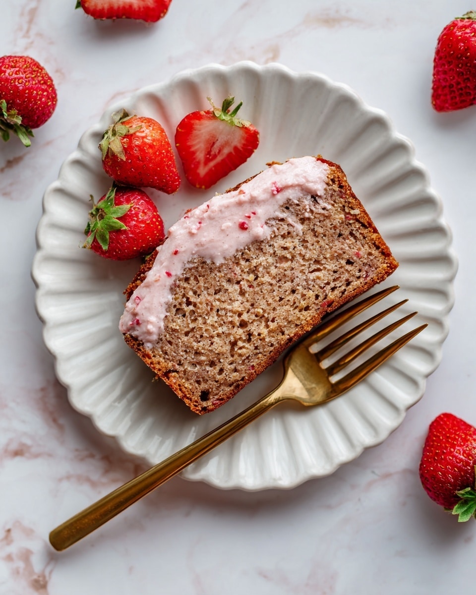 A slice of moist brown bread with visible small seeds and a slightly rough texture sits on a white scalloped plate. The top layer of the bread has a thin spread of pink cream with tiny red bits sprinkled on it. Surrounding the plate are fresh, halved strawberries showing their bright red flesh and tiny seeds, adding a fresh, juicy contrast. A golden fork is placed near the bottom right of the plate on a white marbled surface. Photo taken with an iphone --ar 4:5 --v 7