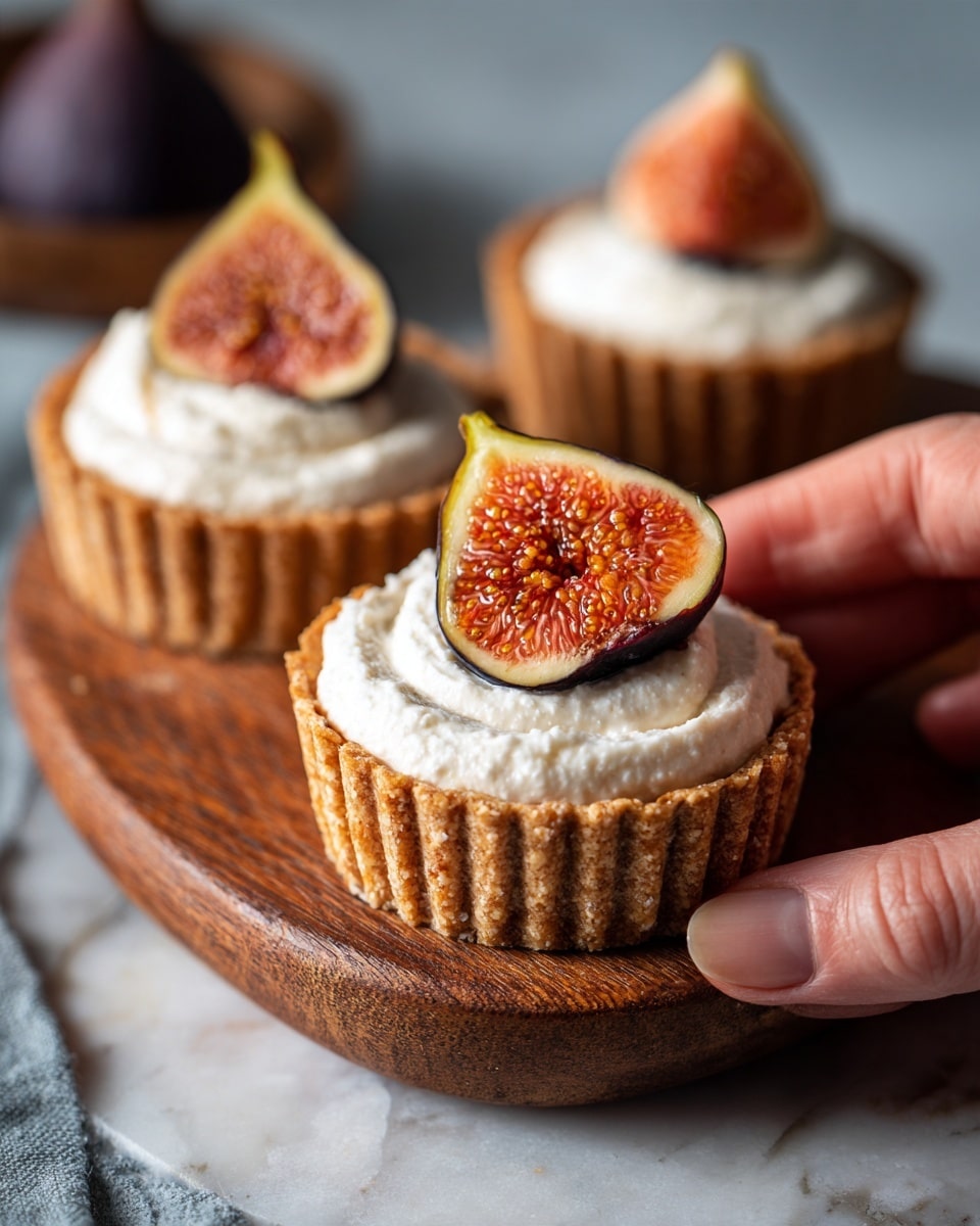 The image shows small tart cups with three visible layers. The bottom layer is a light golden brown crust that looks crisp and fluted around the edges. The middle layer is a thick, smooth, and creamy white filling that fills the tart shell almost to the top. The top layer consists of a halved dark purple fig with visible seeds, placed centrally on the creamy layer, adding texture and a natural, fresh look. The tarts are arranged on a wooden surface, and a woman's hand is gently holding one tart in the foreground. The background has a soft focus of more tarts. photo taken with an iphone --ar 4:5 --v 7